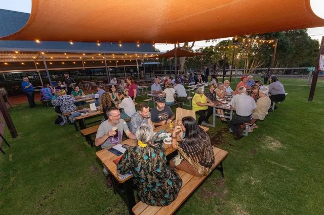 Guests dining outdoors at picnic tables under lights